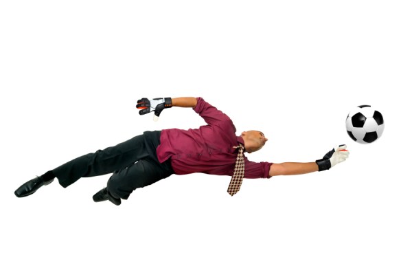 Businessman goalkeeper with gloves  in a acrobatic pose with a soccer ball isolated in white